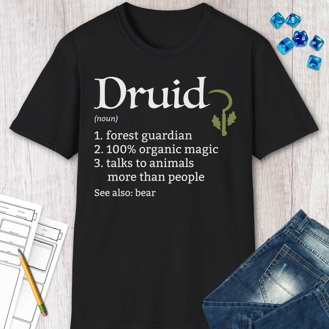The black Druid class definition shirt laid flat beside blue dice, a notepad and folded jeans.