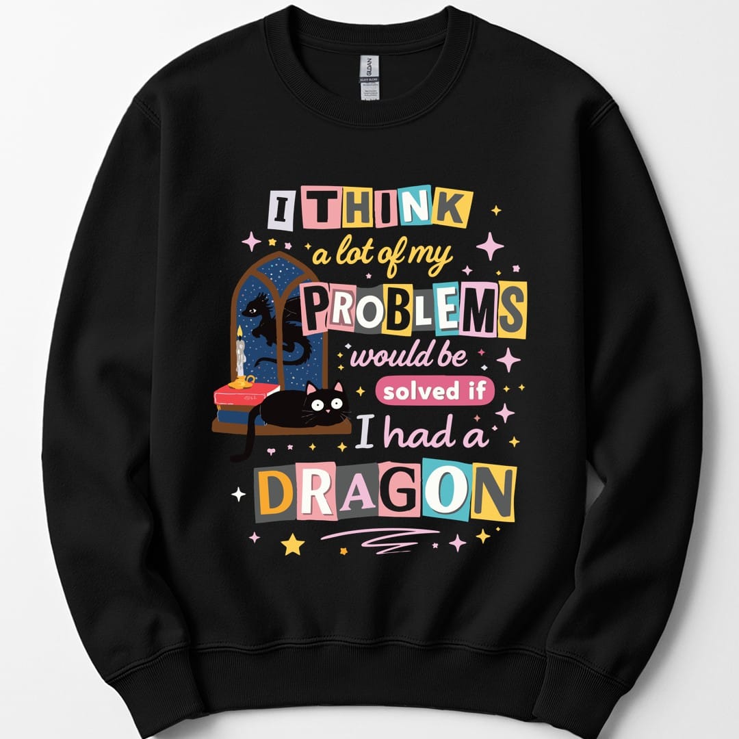 Black sweatshirt. Reads "I think a lot of my problems would be solved if I had a dragon" in ransom-note style, each word on its own colored tile in pink, blue, yellow and cream. Behind the words sits a black cat on a windowsill beside a stack of books and an arched window.