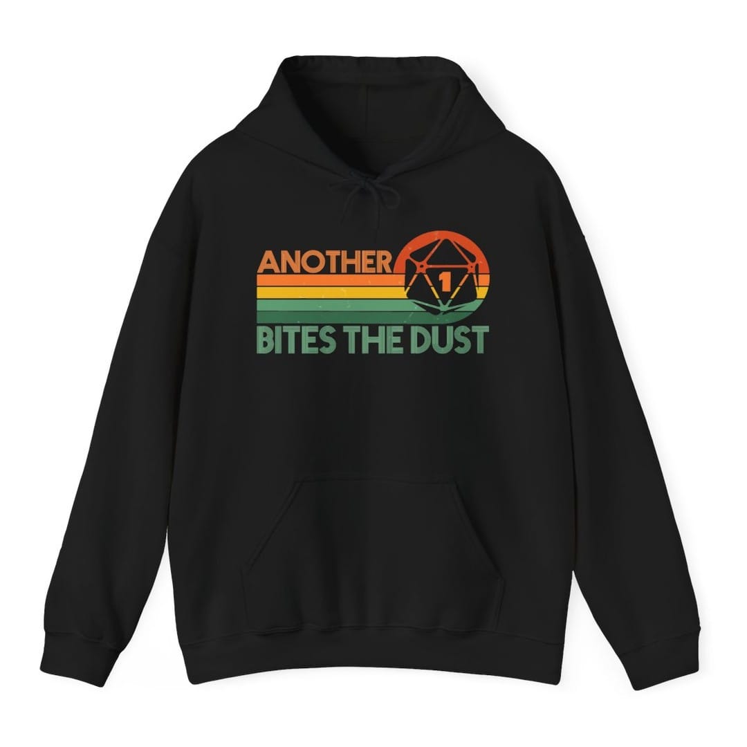 Black hoodie. Reads "Another" in orange capitals across the top and "Bites the dust" in green capitals across the bottom, with retro stripes in orange, yellow and green running between them. A large twenty-sided die showing 1 sits at the top right.