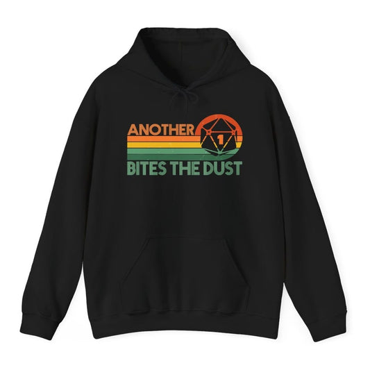 Black hoodie. Reads "Another" in orange capitals across the top and "Bites the dust" in green capitals across the bottom, with retro stripes in orange, yellow and green running between them. A large twenty-sided die showing 1 sits at the top right.