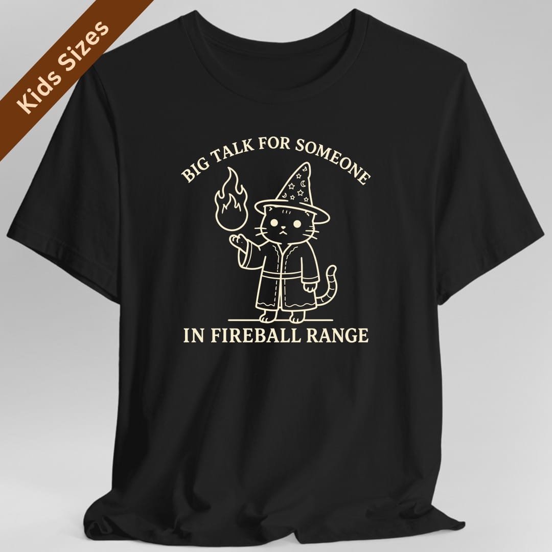 Black kids t-shirt. Reads "Big talk for someone" curving across the top and "In fireball range" across the bottom in cream capitals. Between them a cat stands upright in a starry pointed hat and robe, looking unimpressed, holding up a small flame in one paw.