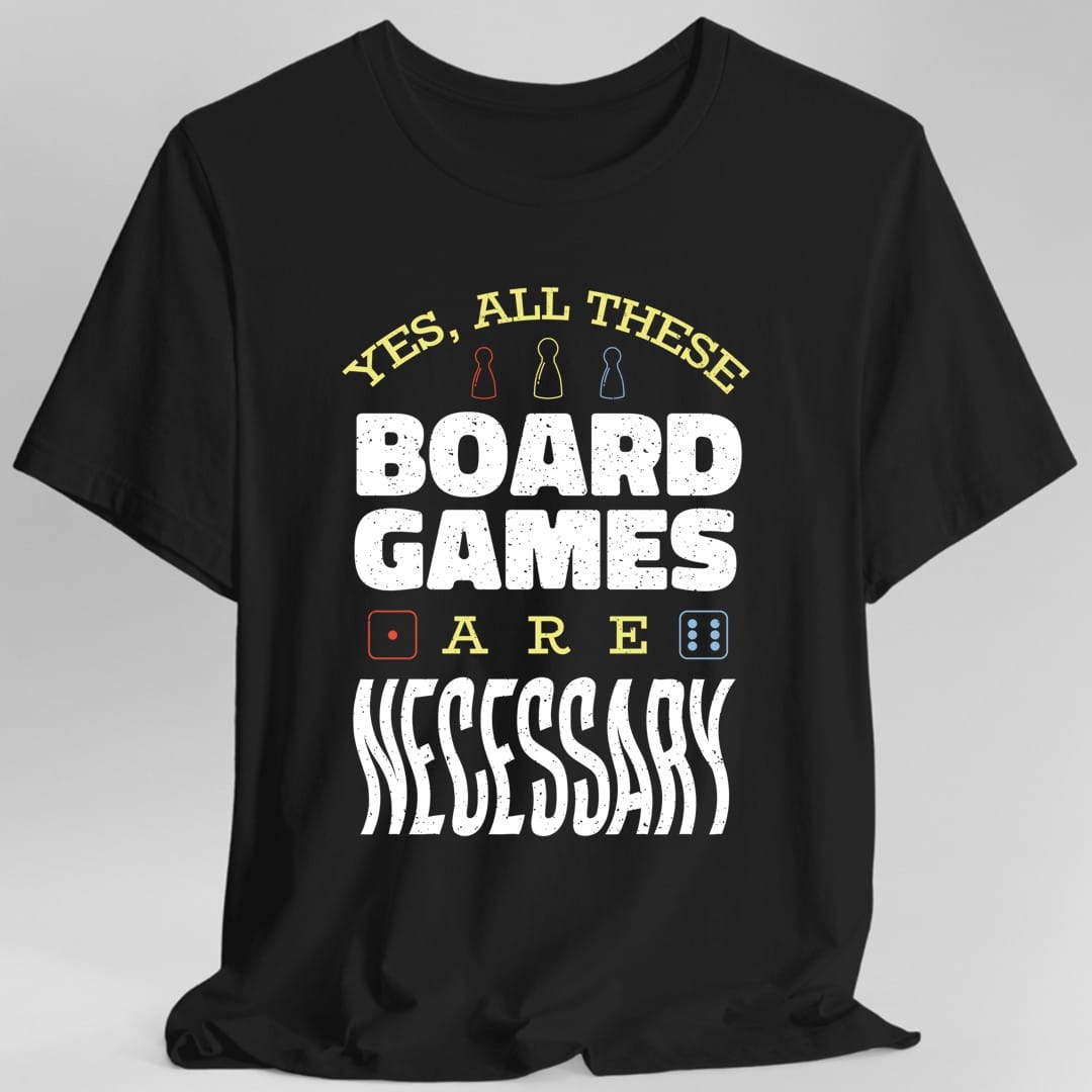 Black t-shirt. Reads "Yes, all these" across the top in gold capitals with three small meeples between the words, then "Board games" in large white capitals, then "Are" with a small red and a small blue die either side, and "Necessary" in large white letters at the bottom.