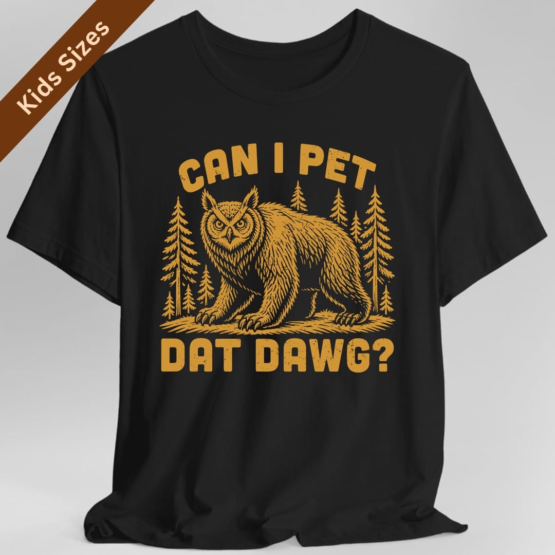 Black kids t-shirt. The design reads "Can I pet dat dawg?" in chunky arched capitals, split above and below the picture. Between them a shaggy owlbear, part great horned owl and part bear, stands on all fours on a patch of ground with tall pine trees behind it. Retro woodcut style, printed in a single warm gold ink.