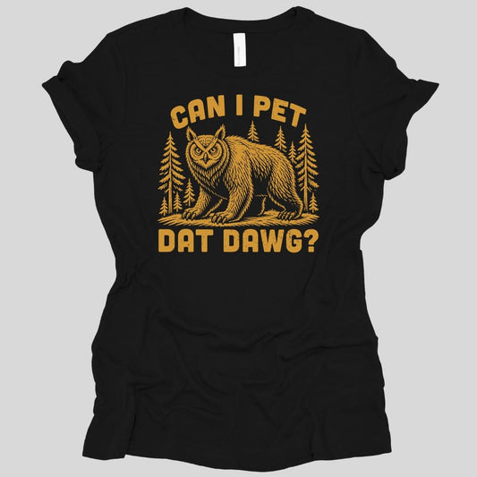 Black women's t-shirt. The design reads "Can I pet dat dawg?" in chunky arched capitals, split above and below the picture. Between them a shaggy owlbear, part great horned owl and part bear, stands on all fours on a patch of ground with tall pine trees behind it. Retro woodcut style, printed in a single warm gold ink.