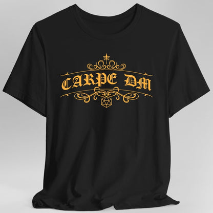 Black t-shirt. Reads "Carpe DM" in a large ornate serif with long curling flourishes sweeping out either side and above. A small twenty-sided die outline sits centered beneath the words. Fine decorative line work, all in a single warm gold.