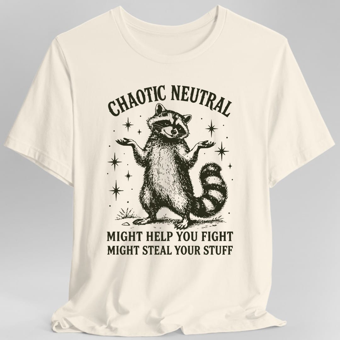 Natural t-shirt. Reads "Chaotic Neutral" curving across the top in dark green capitals. Below, a raccoon stands upright with both paws spread in a shrug, drawn in fine engraving lines and ringed with sparkles. At the bottom, "Might help you fight, might steal your stuff." One dark green ink.