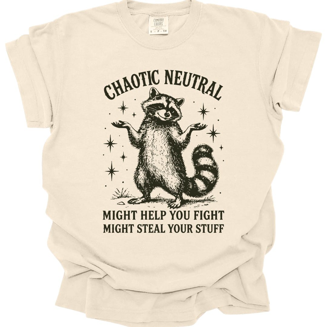 Ivory t-shirt. Reads "Chaotic Neutral" curving across the top in dark green capitals. Below, a raccoon stands upright with both paws spread in a shrug, drawn in fine engraving lines and ringed with sparkles. At the bottom, "Might help you fight, might steal your stuff." One dark green ink.