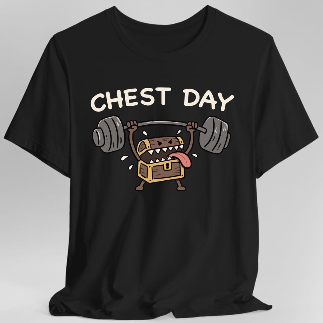 Black t-shirt. The design reads "CHEST DAY" in chunky cream letters arched across the top. Below, a cartoon treasure chest mimic stands on two stubby legs and presses a heavy barbell overhead with both arms. Its lid gapes open like a mouth, showing rows of white triangular teeth, angry slanted eyes and a pink tongue lolling out one side, with sweat drops flying off. The chest is brown wood with gold banding and a keyhole, in a bold black-outlined doodle style.