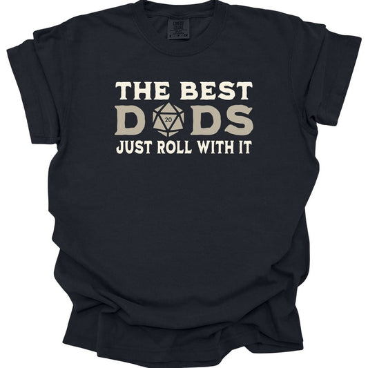 Black t-shirt. Reads "The best" across the top in cream capitals, then "Dads" in large letters where the middle letter is replaced by a twenty-sided die showing 20. Across the bottom, "Just roll with it". All type in cream and tan.