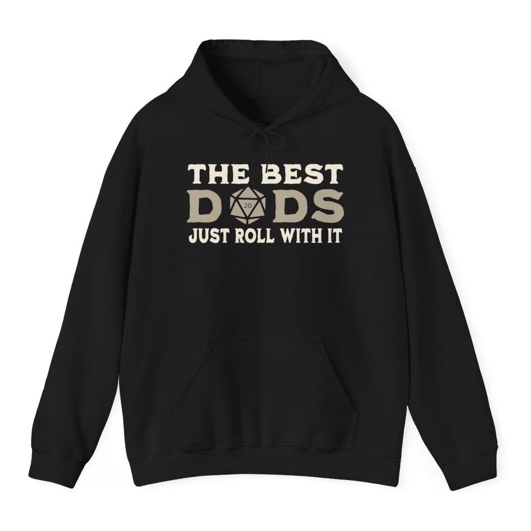 Black hoodie. Reads "The best" across the top in cream capitals, then "Dads" in large letters where the middle letter is replaced by a twenty-sided die showing 20. Across the bottom, "Just roll with it". All type in cream and tan.