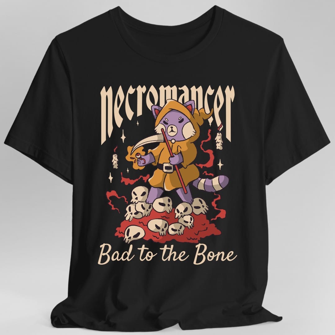 Black t-shirt. Reads "Necromancer" across the top in an ornate blackletter and "Bad to the bone" in cream script across the bottom. Between them a purple cat in a gold hooded robe stands on a heap of skulls, holding a scythe in one paw and a lit candle in the other.