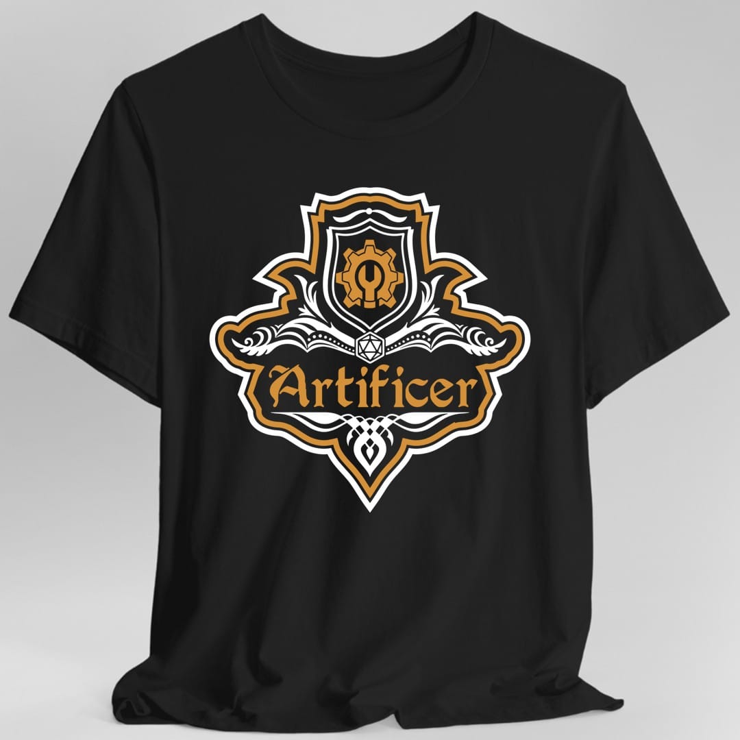 Black t-shirt. A crest shaped like a shield with scalloped edges, outlined in white and amber orange. A small inner shield at the top carries a cogwheel with a keyhole, an open book with a twenty-sided die on it sits across the middle, and a banner below reads "Artificer" in an ornate blackletter script. A pointed pendant hangs from the bottom. White line work with amber orange accents.
