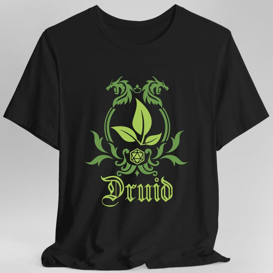 Black t-shirt. A heraldic crest drawn entirely in leaf green on a plain background. Curling vines arch over an arched frame, a sprig of three leaves sits inside it, and a twenty-sided die hangs below between leafy flourishes. Underneath, "Druid" in an ornate blackletter script.