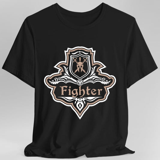 Black t-shirt. A crest shaped like a shield with scalloped edges, outlined in white and dusty rose. A small inner shield at the top carries a helm behind crossed swords, an open book with a twenty-sided die on it sits across the middle, and a banner below reads "Fighter" in an ornate blackletter script. A pointed pendant hangs from the bottom. White line work with dusty rose accents.