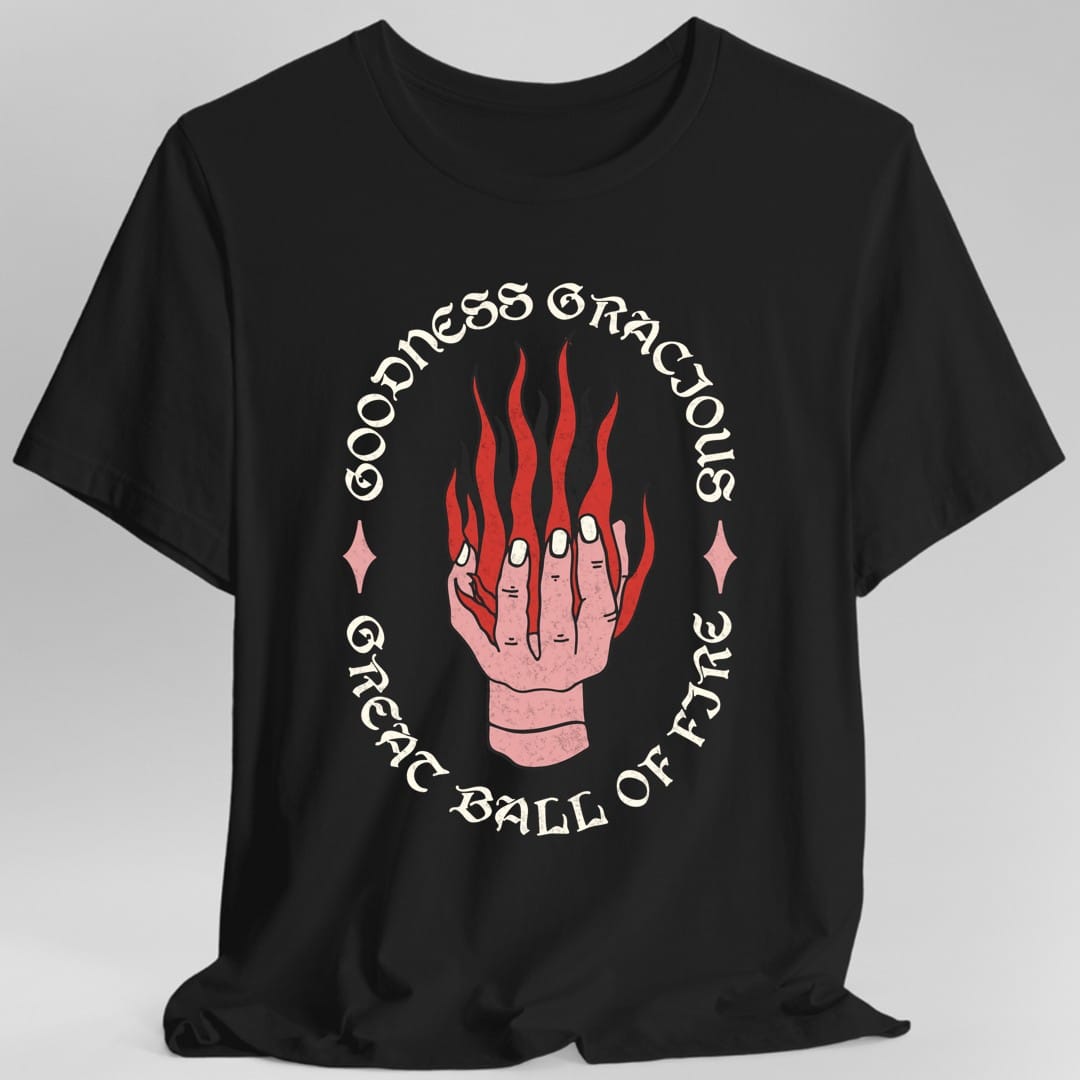 Black t-shirt. A pale hand reaches up from the bottom with flames pouring off its fingers. Around it, curving in a full circle, the words "Goodness gracious great ball of fyre" in an ornate serif, with a small diamond either side. Coral pink and red on a plain background.