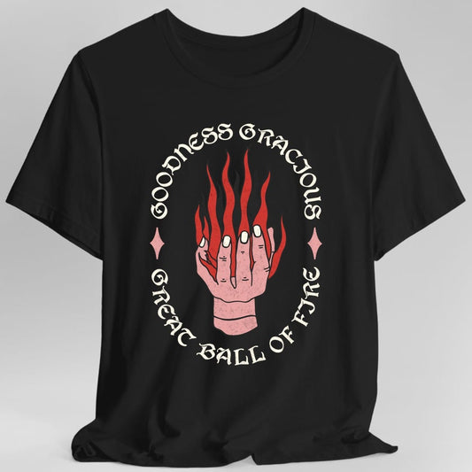 Black t-shirt. A pale hand reaches up from the bottom with flames pouring off its fingers. Around it, curving in a full circle, the words "Goodness gracious great ball of fyre" in an ornate serif, with a small diamond either side. Coral pink and red on a plain background.