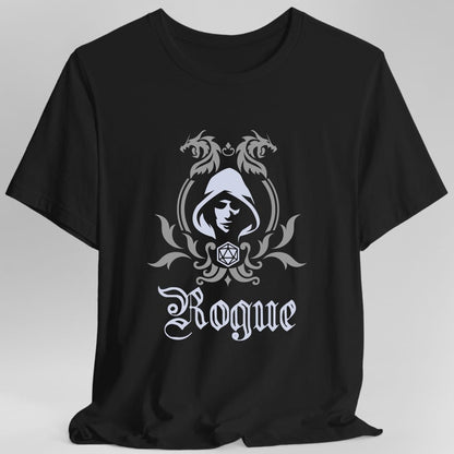 Black t-shirt. A heraldic crest drawn entirely in silver gray on a plain background. Two dragons face each other over an arched frame, a hooded face in shadow sits inside the arch, and a twenty-sided die hangs below it between leafy flourishes. Underneath, "Rogue" in an ornate blackletter script.