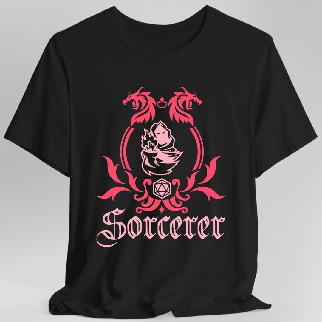Black t-shirt. A heraldic crest drawn entirely in hot pink and crimson on a plain background. Two dragons face each other over an arched frame, a robed figure casting a spell sits inside the arch, and a twenty-sided die hangs below it between leafy flourishes. Underneath, "Sorcerer" in an ornate blackletter script.