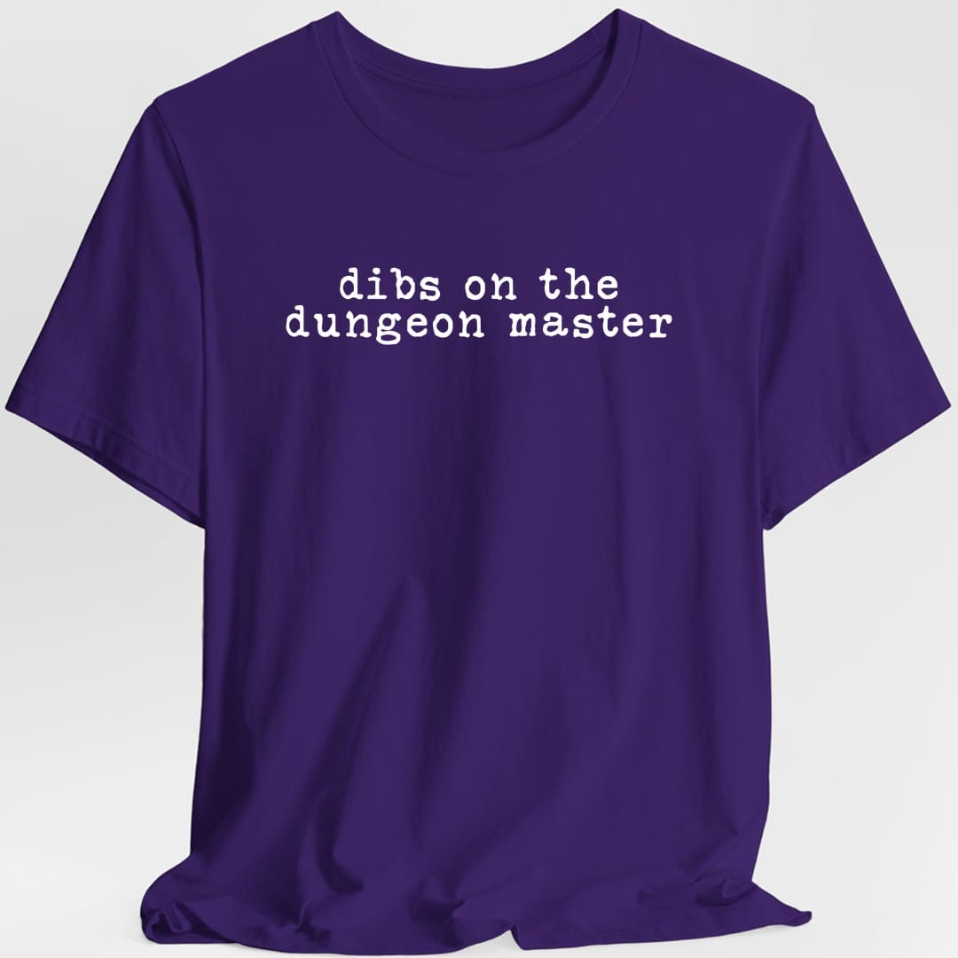 Purple t-shirt. Reads "dibs on the dungeon master" on two lines in plain lowercase typewriter lettering, white on dark colors and black on light ones. Nothing else at all, no illustration, just the words centered on the chest.