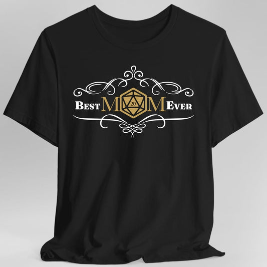 Black t-shirt. Reads "Best" and "Ever" either side of "MOM" in the centre, where the letter O is replaced by a gold twenty-sided die showing 20. Curling white filigree flourishes arch above and below the words. Small and centred, in white and gold.