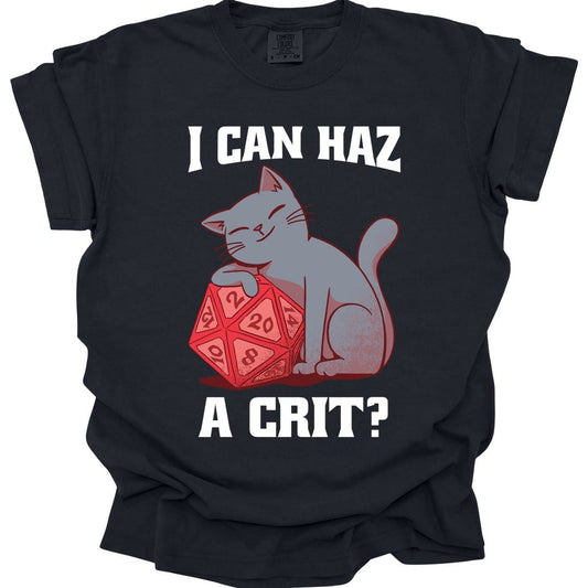 Black t-shirt. Reads "I can haz" across the top and "A crit?" across the bottom in bold white capitals. Between them a gray cat sits with its eyes closed and one paw resting on top of a large red twenty-sided die showing 20. Simple flat cartoon style.