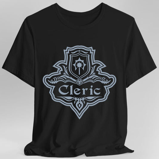 Black t-shirt. A crest shaped like a shield with scalloped edges, drawn entirely in pale slate blue with no other color. A small inner shield at the top carries a winged holy symbol, an open book with a twenty-sided die on it sits across the middle, and a banner below reads "Cleric" in an ornate blackletter script. A pointed pendant hangs from the bottom.