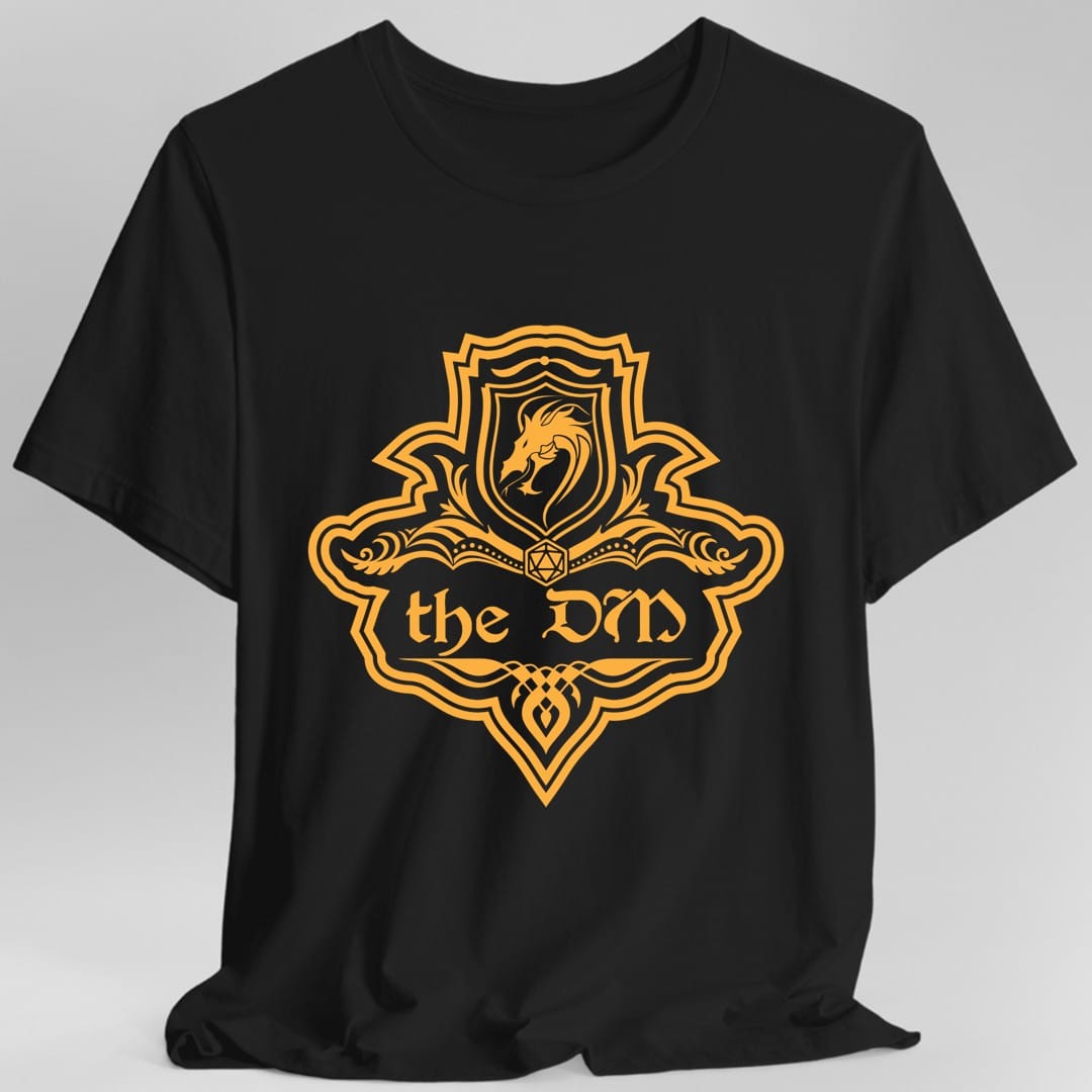Black t-shirt. A crest shaped like a shield with scalloped edges, drawn entirely in amber orange with no other color. A small inner shield at the top carries a rearing dragon, an open book with a twenty-sided die on it sits across the middle, and a banner below reads "the DM" in an ornate blackletter script. A pointed pendant hangs from the bottom.