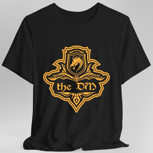 Black t-shirt. A crest shaped like a shield with scalloped edges, drawn entirely in amber orange with no other color. A small inner shield at the top carries a rearing dragon, an open book with a twenty-sided die on it sits across the middle, and a banner below reads "the DM" in an ornate blackletter script. A pointed pendant hangs from the bottom.