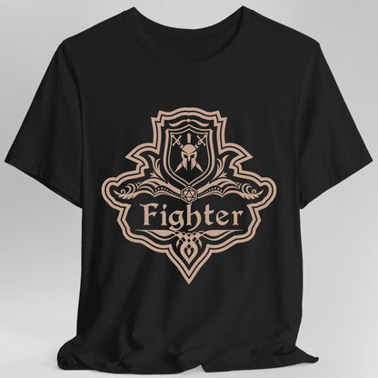 Black t-shirt. A crest shaped like a shield with scalloped edges, drawn entirely in dusty rose with no other color. A small inner shield at the top carries a helm behind crossed swords, an open book with a twenty-sided die on it sits across the middle, and a banner below reads "Fighter" in an ornate blackletter script. A pointed pendant hangs from the bottom.
