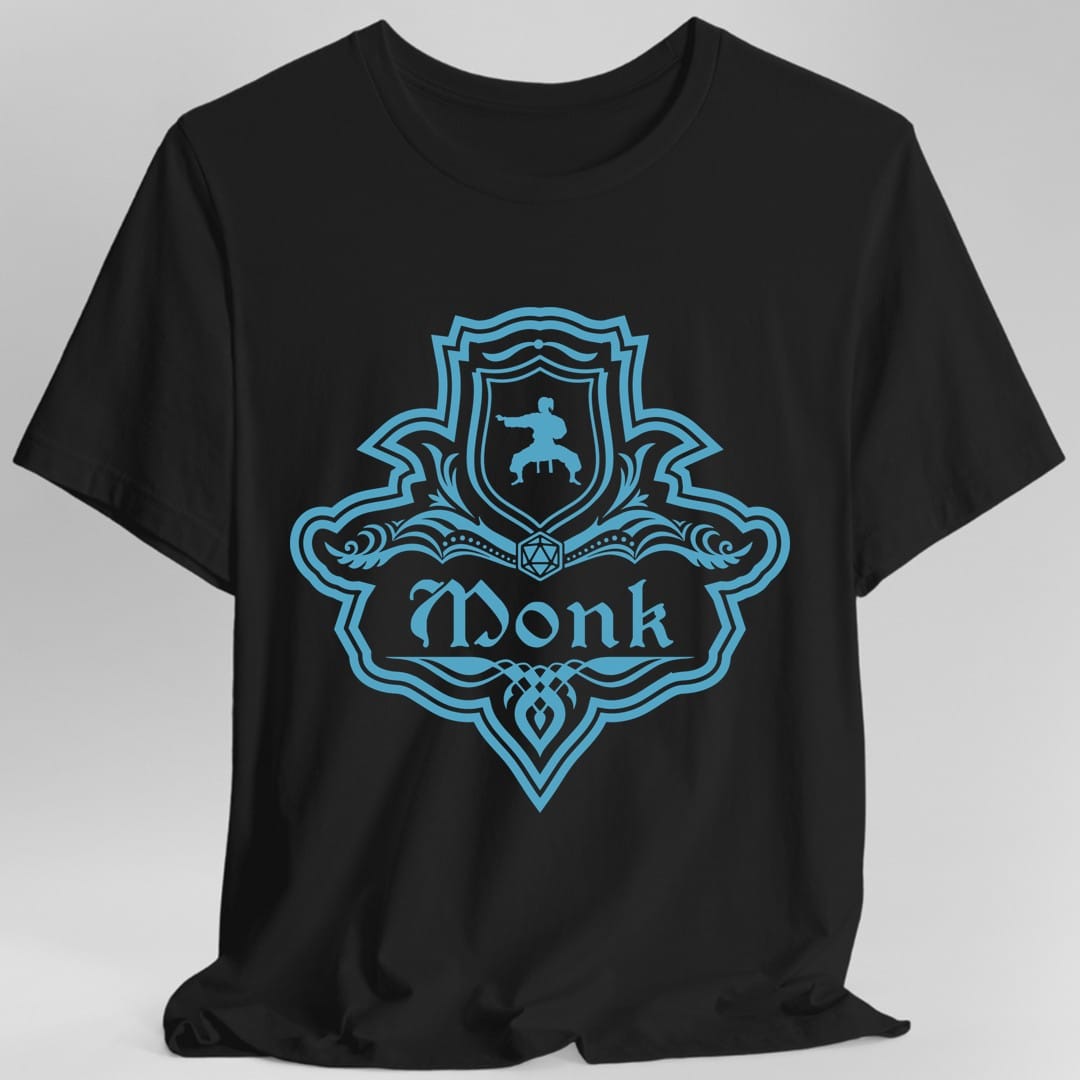 Black t-shirt. A crest shaped like a shield with scalloped edges, drawn entirely in bright teal with no other color. A small inner shield at the top carries a figure mid martial arts kick, an open book with a twenty-sided die on it sits across the middle, and a banner below reads "Monk" in an ornate blackletter script. A pointed pendant hangs from the bottom.