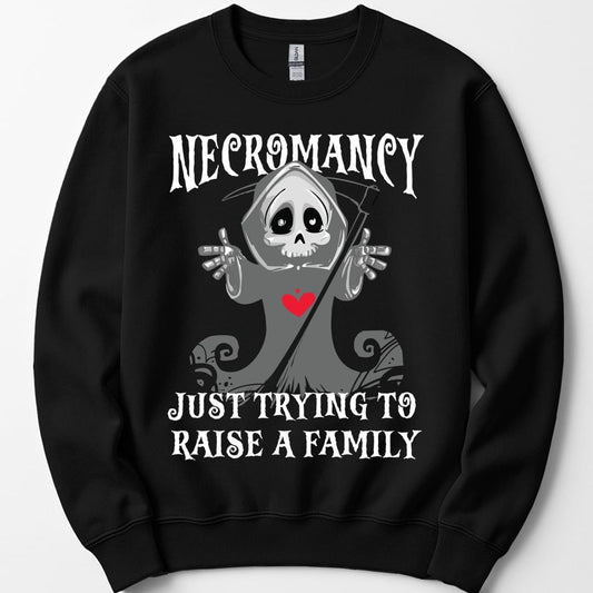 Black sweatshirt. Reads "Necromancy" across the top and "Just trying to raise a family" across the bottom in white spooky capitals. Between them a small cartoon grim reaper in a gray hood holds up both bony hands with a friendly wide-eyed skull face and a red heart on its chest, a scythe leaning behind it. Cute rather than scary. Grays and white with the one red heart.