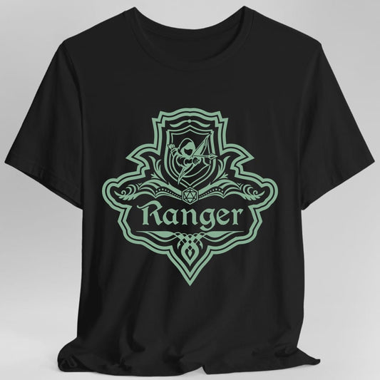 Black t-shirt. A crest shaped like a shield with scalloped edges, drawn entirely in sage green with no other color. A small inner shield at the top carries an archer drawing a bow, an open book with a twenty-sided die on it sits across the middle, and a banner below reads "Ranger" in an ornate blackletter script. A pointed pendant hangs from the bottom.