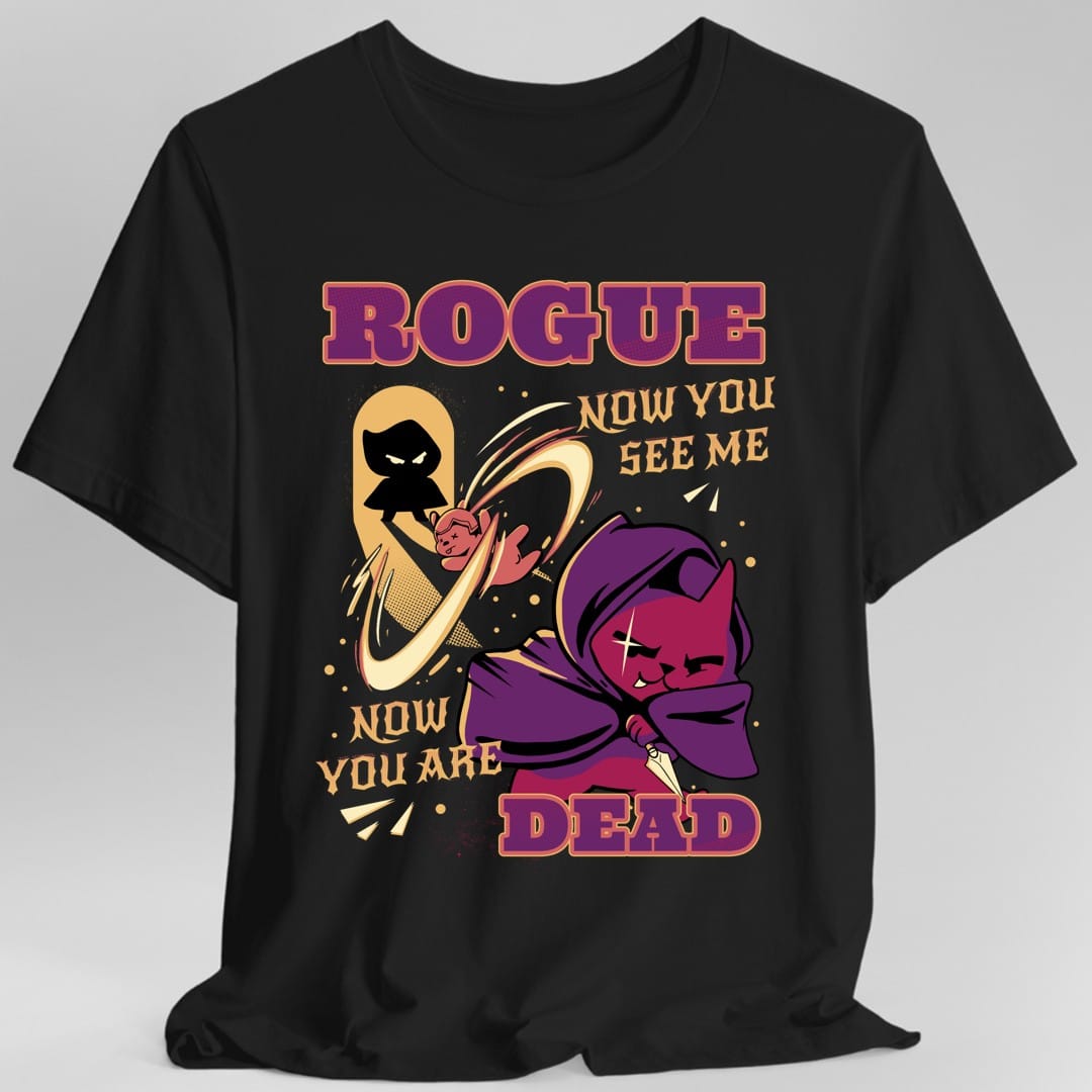 Black t-shirt. Reads "Rogue" across the top in purple and gold capitals, with "Now you see me" to the right and "Now you are dead" at the bottom in cream. In the middle a small pink cat in a purple hooded cloak holds a dagger, with its own black silhouette swirling away behind it.