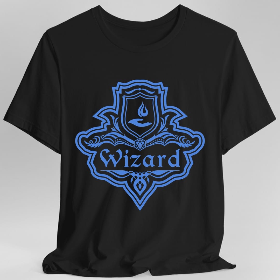 Black t-shirt. A crest shaped like a shield with scalloped edges, drawn entirely in cornflower blue with no other color. A small inner shield at the top carries a flame in a cupped hand, an open book with a twenty-sided die on it sits across the middle, and a banner below reads "Wizard" in an ornate blackletter script. A pointed pendant hangs from the bottom.