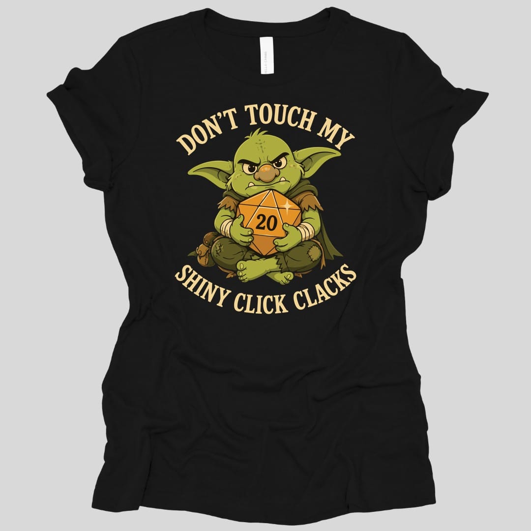 Black women's t-shirt. Reads "Don't touch my" curving across the top and "Shiny click clacks" across the bottom in cream capitals. Between them a green goblin sits scowling and hugging a large orange twenty-sided die showing 20 to its chest with both arms.