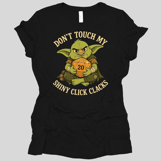 Black women's t-shirt. Reads "Don't touch my" curving across the top and "Shiny click clacks" across the bottom in cream capitals. Between them a green goblin sits scowling and hugging a large orange twenty-sided die showing 20 to its chest with both arms.