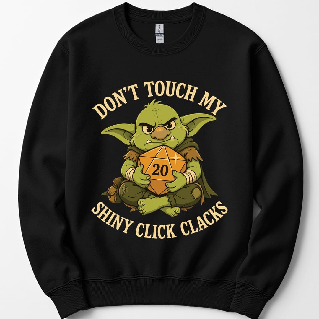Black sweatshirt. Reads "Don't touch my" curving across the top and "Shiny click clacks" across the bottom in cream capitals. Between them a green goblin sits scowling and hugging a large orange twenty-sided die showing 20 to its chest with both arms.