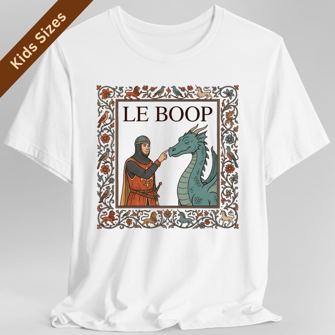 White kids t-shirt. The design reads "Le Boop" in serif capitals at the top of a framed panel, styled like a page from an illuminated manuscript. Inside the panel a knight in chainmail and an orange fleur-de-lis surcoat reaches out and touches the snout of a green dragon, which has its eyes closed. A thick decorated border of vines, orange and blue flowers, lions, unicorns and birds runs all the way around. Medieval manuscript art in orange, teal, gold and brown.
