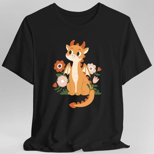 Black t-shirt. A round orange baby dragon sits facing forward with its long tail curled across the front, small cream wings out and short ridged horns on its head. It has big dark eyes and pink cheeks. Around it grow daisies and tulips in rust orange and blush pink among green leaves and grass. Soft flat cartoon illustration, no words.