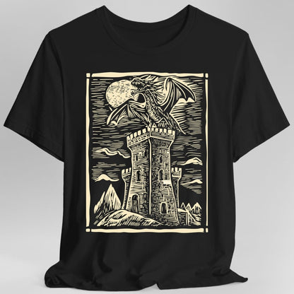 Black t-shirt. A square framed woodcut scene: a dragon with spread wings perches on top of a tall stone tower, with a full moon behind it and mountains and a hatched sky beyond. Carved line work throughout, all in a single cream. No words.