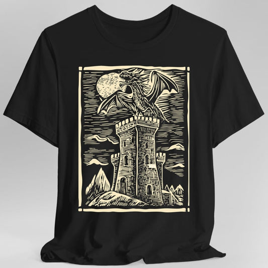 Black t-shirt. A square framed woodcut scene: a dragon with spread wings perches on top of a tall stone tower, with a full moon behind it and mountains and a hatched sky beyond. Carved line work throughout, all in a single cream. No words.