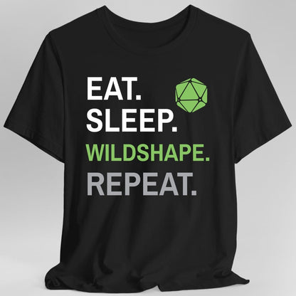 Black t-shirt. Four words stacked in heavy block capitals on four lines: "Eat." and "Sleep." in white, then "Wildshape." in leaf green, then "Repeat." in gray. A leaf green twenty-sided die sits in the top right corner beside the word Eat. All type, no illustration.