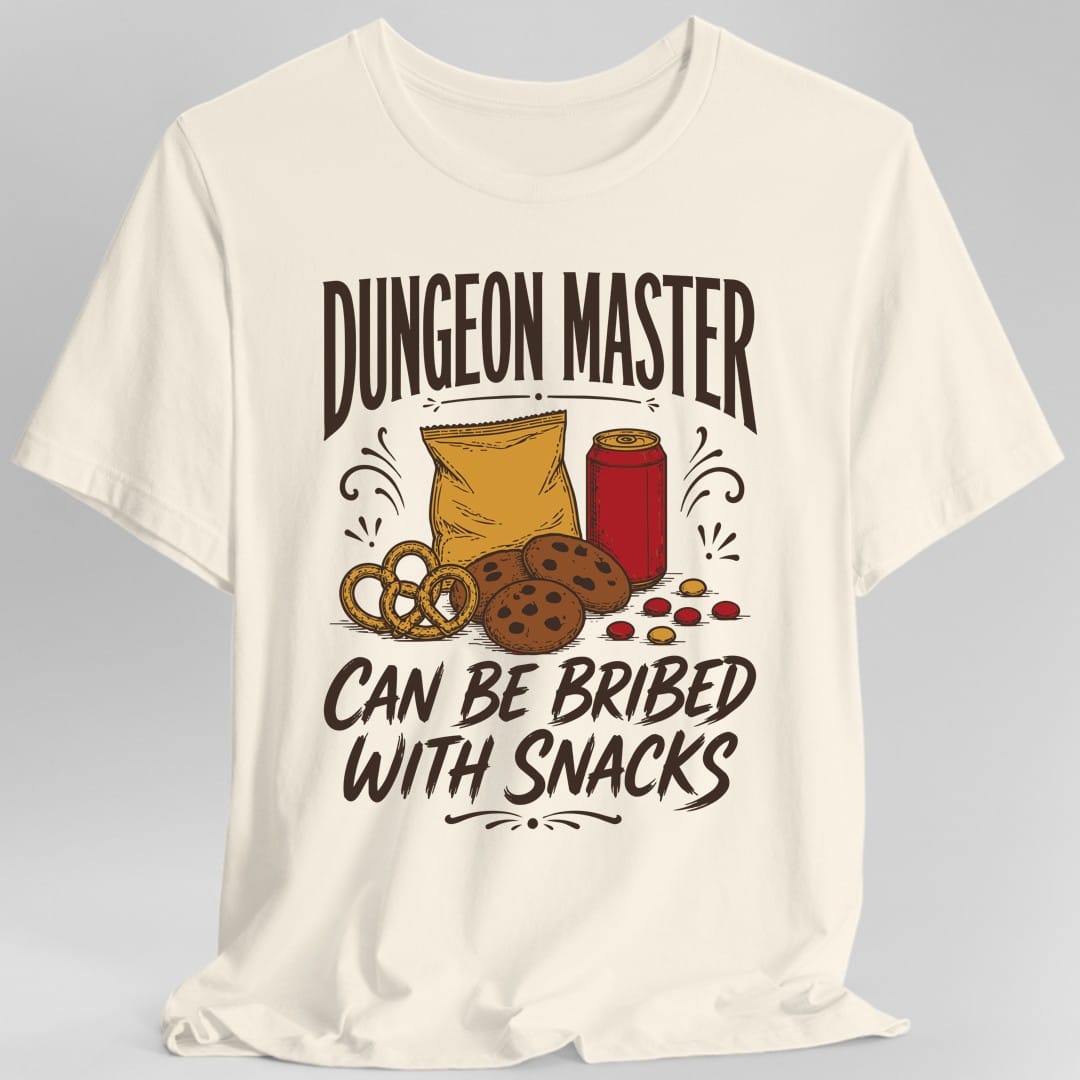 Natural t-shirt. The design reads DUNGEON MASTER across the top and CAN BE BRIBED WITH SNACKS across the bottom in tall vintage lettering with curled flourishes. Between them sits a spread of snacks, a bag of chips, a red soda can, chocolate chip cookies, a soft pretzel and scattered candies. Drawn in warm retro label style.