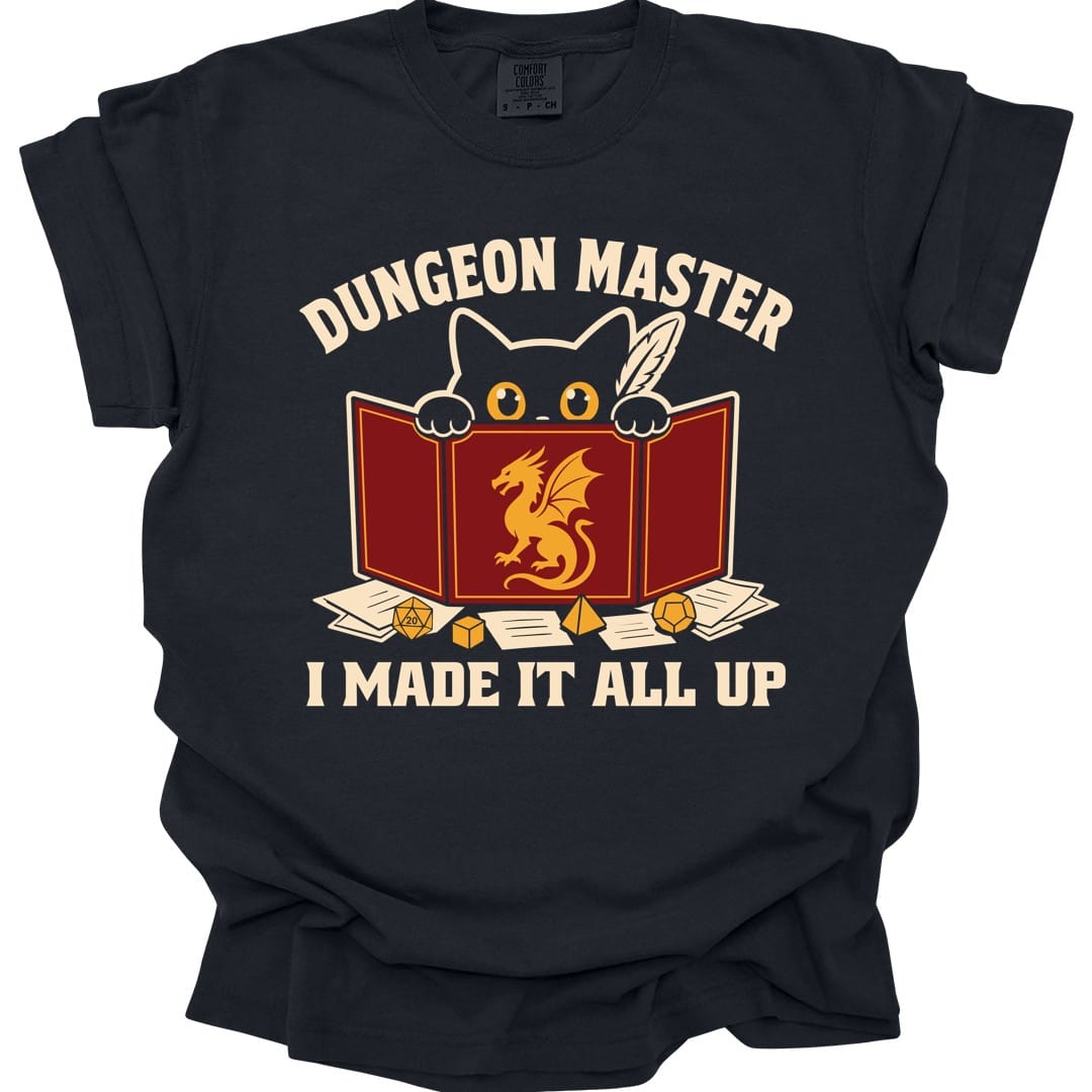 Black t-shirt. Reads "Dungeon Master" curving across the top in cream capitals. Below, a white cat peers over the top of a dark red dungeon master screen with a gold dragon printed on it, paws hooked over the edge, papers and dice scattered around. Across the bottom, "I made it all up".