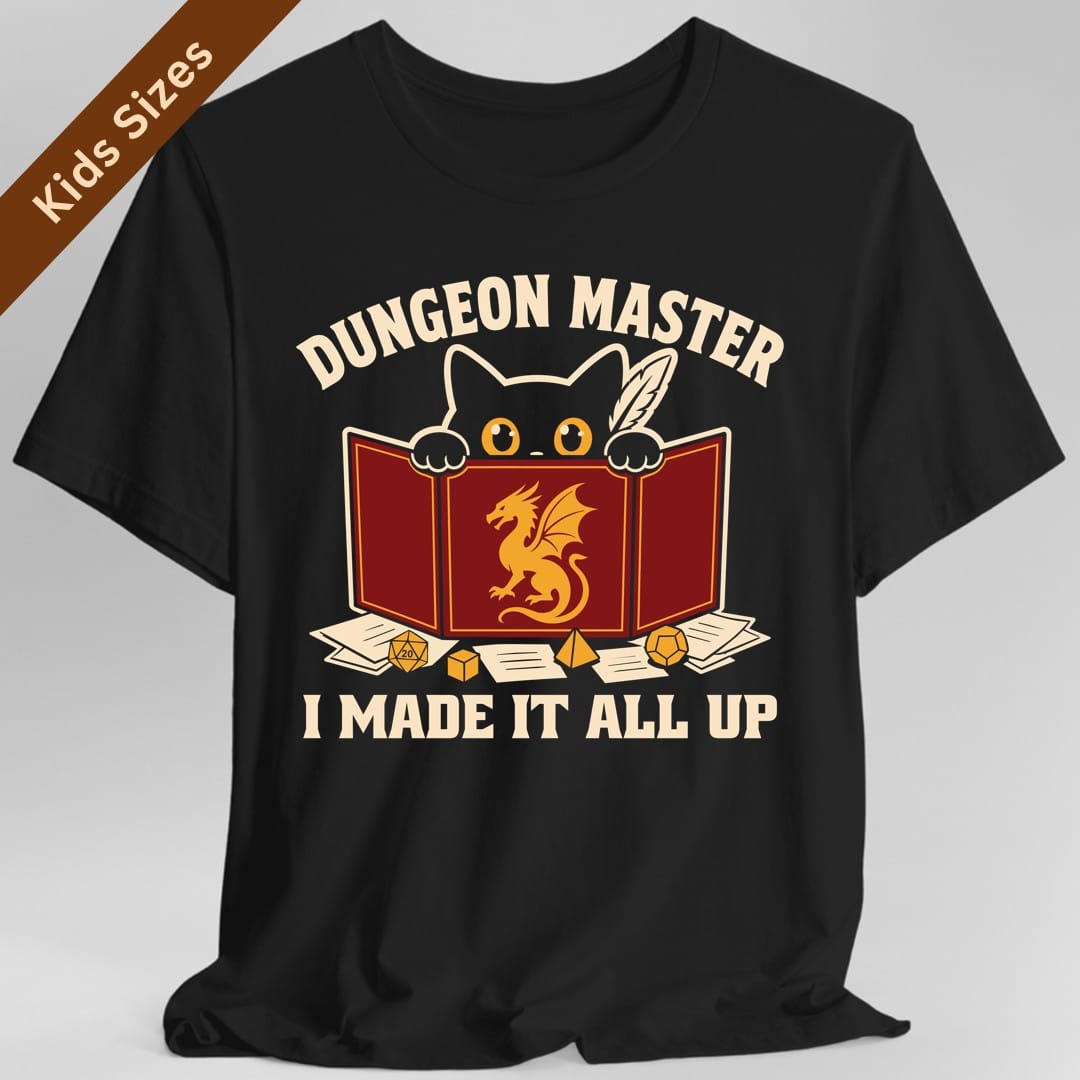 Black kids t-shirt. Reads "Dungeon Master" curving across the top in cream capitals. Below, a white cat peers over the top of a dark red dungeon master screen with a gold dragon printed on it, paws hooked over the edge, papers and dice scattered around. Across the bottom, "I made it all up".