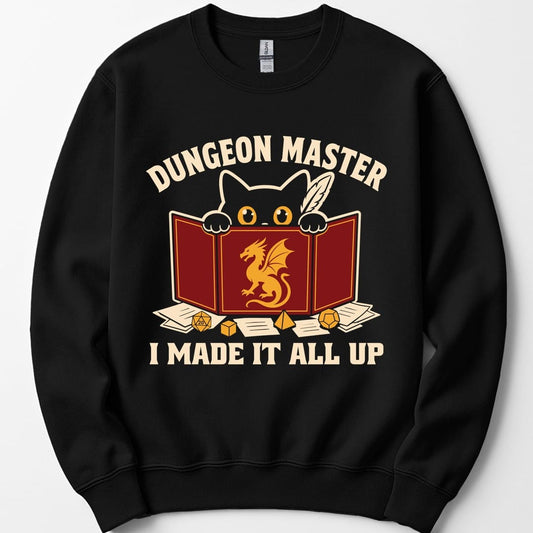 Black sweatshirt. Reads "Dungeon Master" curving across the top in cream capitals. Below, a white cat peers over the top of a dark red dungeon master screen with a gold dragon printed on it, paws hooked over the edge, papers and dice scattered around. Across the bottom, "I made it all up".
