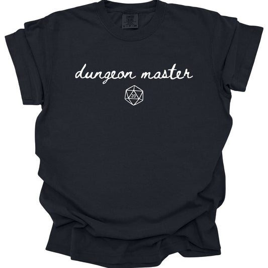 Black t-shirt. Reads "dungeon master" in a flowing white handwritten script across the chest, with a small white twenty-sided die outline centered just below it. Very minimal, nothing else on the shirt.