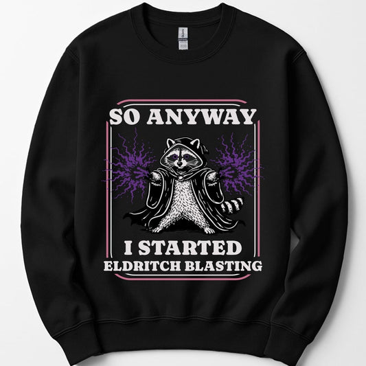 Black sweatshirt. Reads "So anyway" across the top in cream capitals and "I started eldritch blasting" across the bottom. Between them a raccoon sits in a dark hooded cloak with both paws raised and purple magic crackling out. A thin pink and cream double frame runs around the whole design.