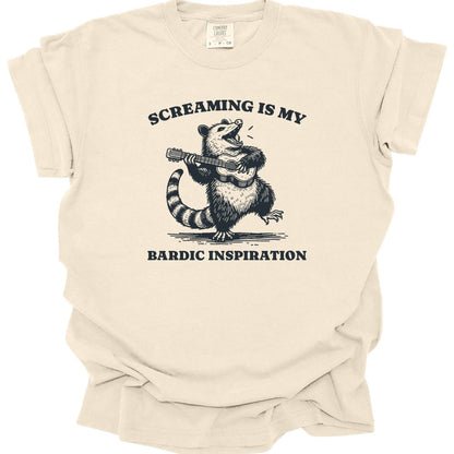Ivory t-shirt. Reads "Screaming is my" curving across the top and "Bardic inspiration" across the bottom. Between them a possum stands upright playing a lute, head thrown back mid-screech with small motion lines either side. Fine engraved linework in dark gray.