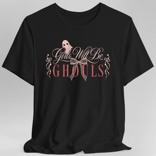 Black t-shirt. Reads "Girls Will Be" in a delicate pink script with "Ghouls" beneath it in larger coral capitals. A small ghost peeks over the top of the lettering, and dainty ribbon bows and strings of beads hang either side. Soft, girlish and pale pink throughout.